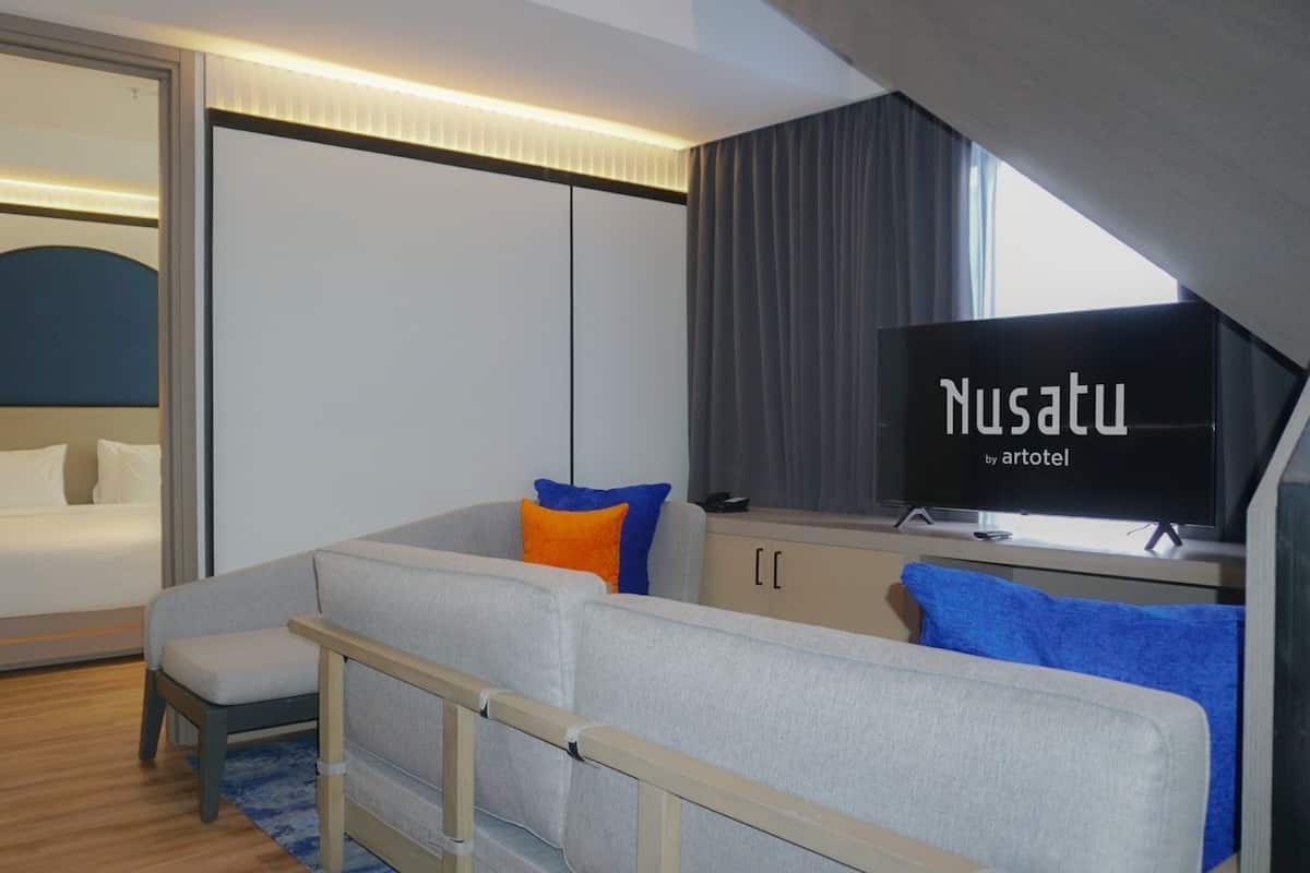 A modern hotel room with a bed, a sofa, a TV, and a desk.