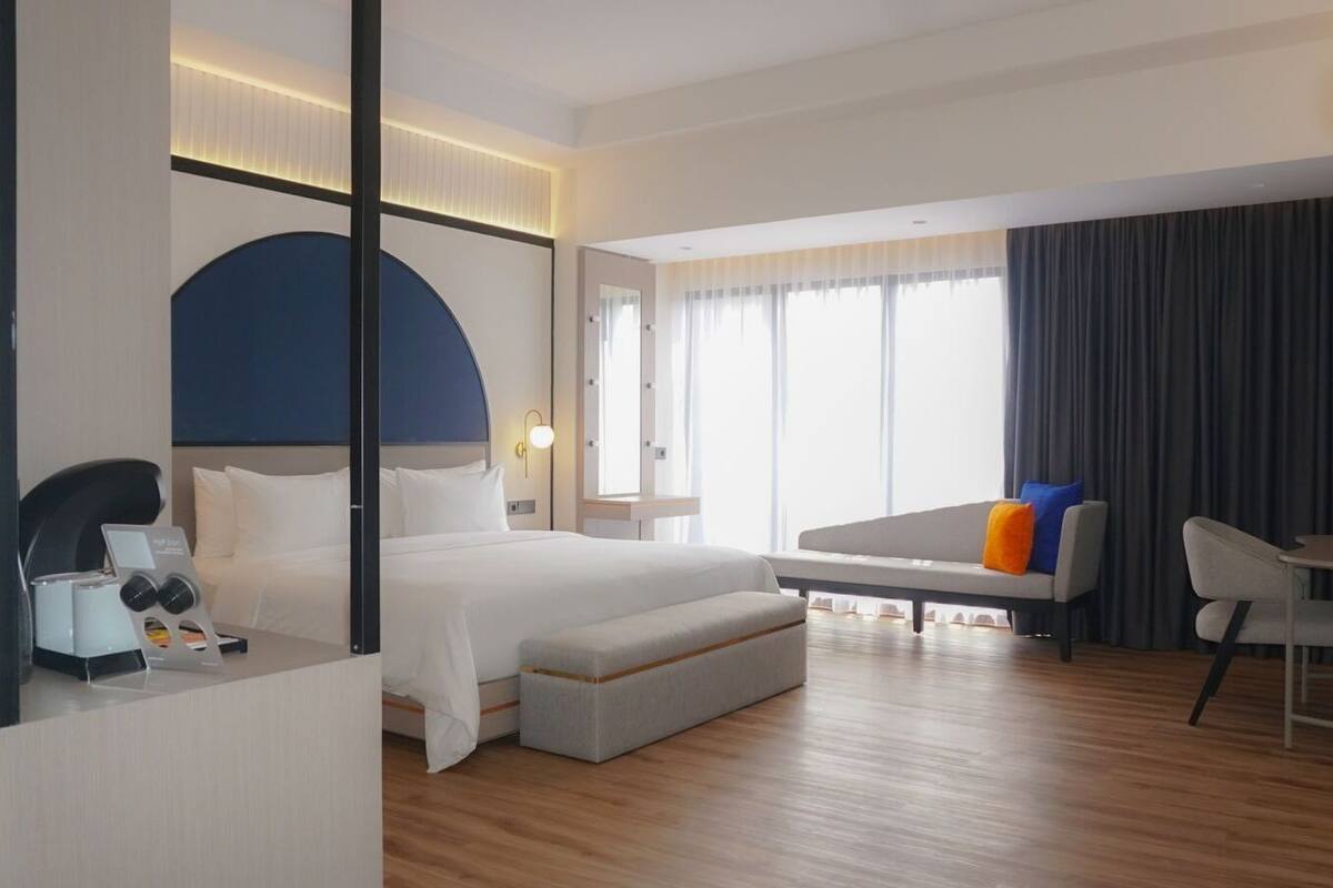 A modern hotel room with a large bed, a sofa, a small table, and a desk.