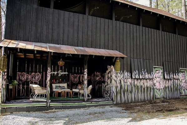 A rustic wooden building with a covered porch, outdoor seating, and a wall mural.