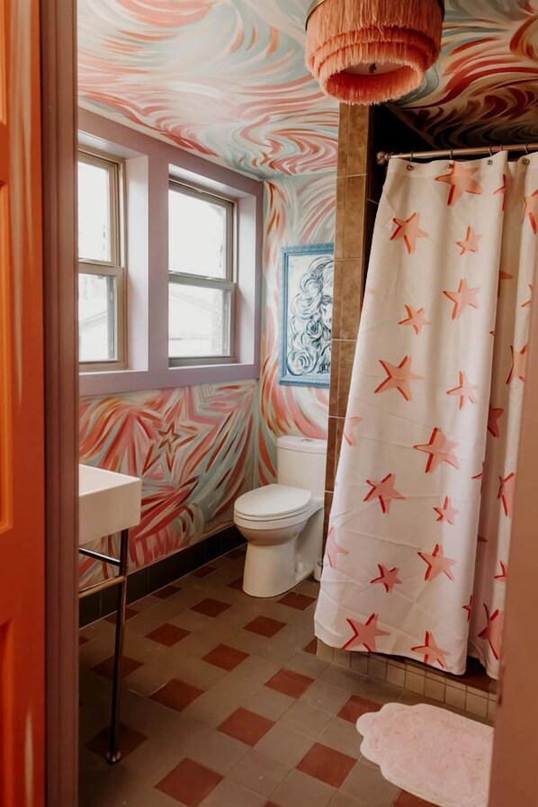 Un baño con techo estampado, una ventana, un inodoro, un lavabo y una cortina de ducha con motivos de estrellas.