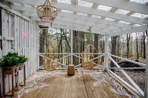 A wooden deck with hanging wicker chairs, a wooden bench, and a potted plant.