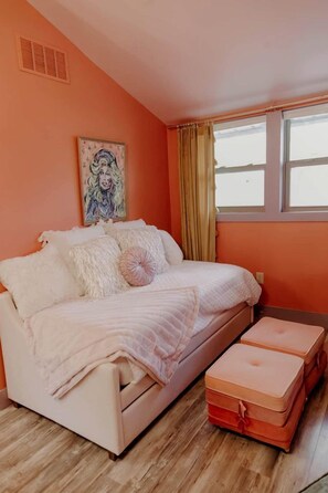 A bedroom with a bed, a window with curtains, a picture on the wall, and a small table.