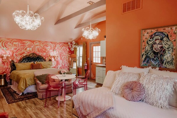 A bedroom with a bed, a desk, chairs, and a painting.