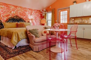 A bedroom with a bed, a sofa, a dining table with chairs, a kitchen area, and a bathroom.