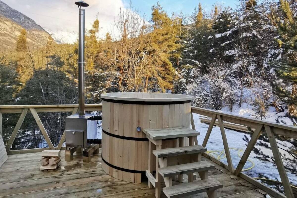 A wooden deck with a sauna, wooden steps, and a view of snow-covered trees and mountains.