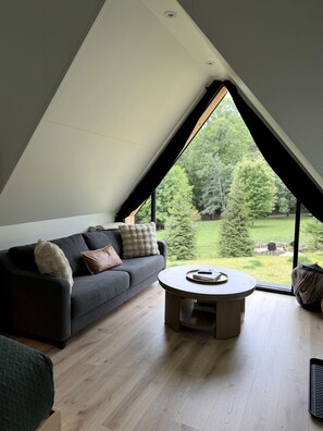 Une pièce avec un plafond en pente, un canapé, une table basse ronde et une vue sur un paysage verdoyant.