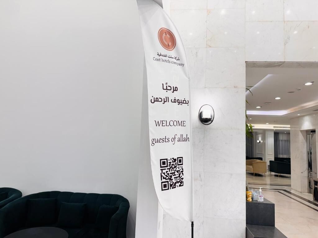 A reception area with a white banner featuring a logo and text in Arabic and English, a QR code, and a modern interior with a seating area and a reception desk.