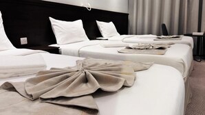 Une chambre d’hôtel avec trois lits, une tête de lit noire et une décoration aux couleurs neutres.