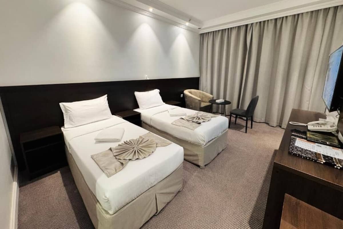 A hotel room with two beds, a desk with a telephone, a chair, and a TV.