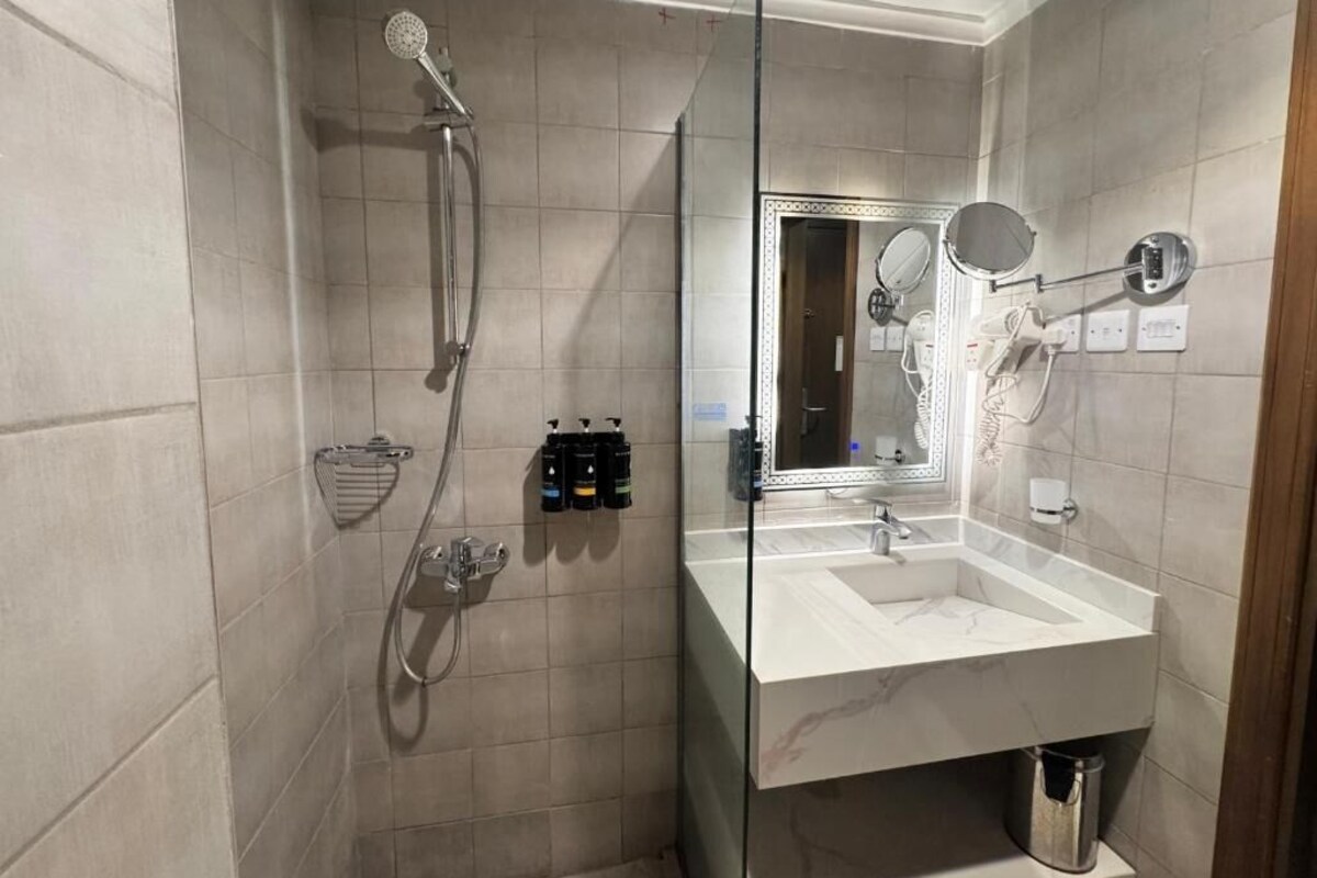 A modern bathroom with a glass-enclosed shower, a large mirror, and a marble sink.
