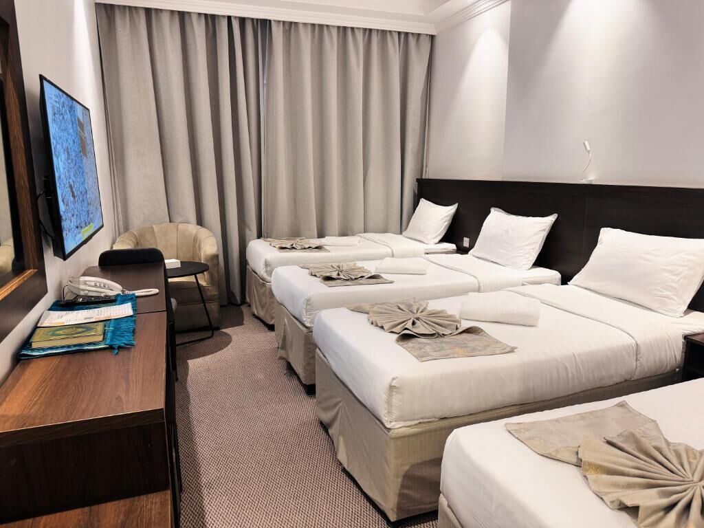 Habitación de hotel con tres camas, un escritorio con teléfono y una silla.