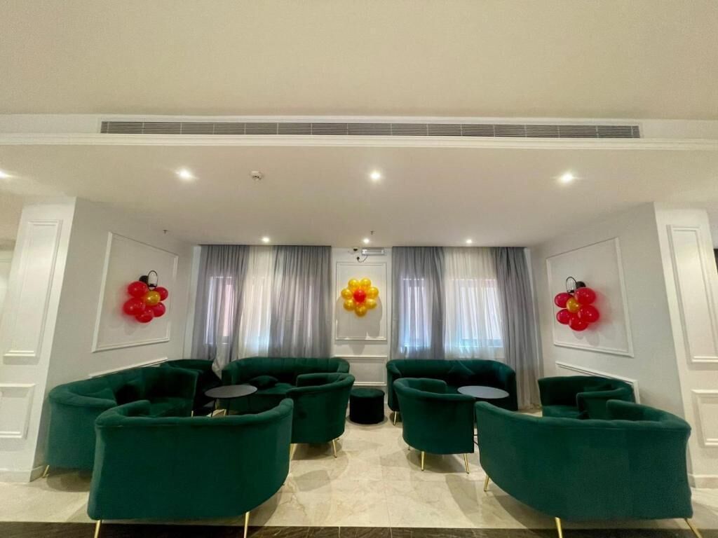 A modern lounge area with green sofas and round tables, white walls, and decorative red and yellow balloon arrangements.