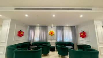 A modern lounge area with green sofas and round tables, white walls, and decorative red and yellow balloon arrangements.