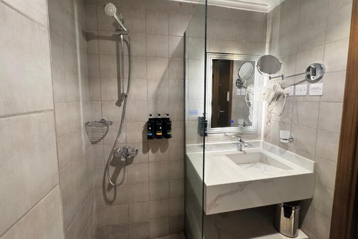 A modern bathroom with a glass-enclosed shower, a large mirror, and a marble sink.