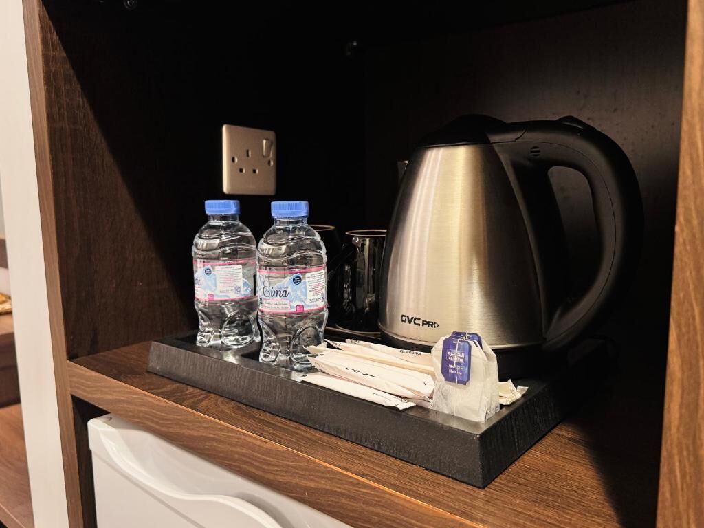Eine Küchenzeile mit einer Edelstahl-Kaffeemaschine, zwei Wasserflaschen und einem Teebeutel auf einer Holzausziehtafel.