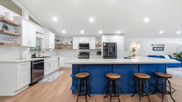 A modern kitchen with white cabinetry, a central island with stools, stainless steel appliances, and a blue accent wall.