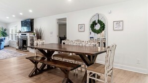 Un comedor con una mesa de madera y sillas blancas, una chimenea y un televisor.