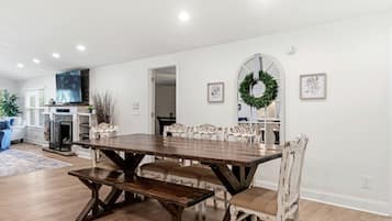 A dining area with a wooden table and white chairs, a fireplace, and a television.