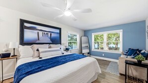 Un dormitorio con cama, ventilador de techo, televisor, ventana con persianas y vistas al exterior.