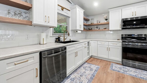 Una cocina moderna con armarios blancos, electrodomésticos de acero inoxidable y piso de madera.