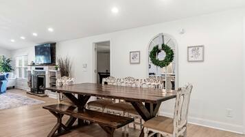A dining area with a wooden table and white chairs, a fireplace, and a television.