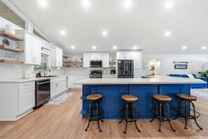A modern kitchen with white cabinetry, a central island with stools, stainless steel appliances, and a blue accent wall. - Ultimate Lakefront Cabin with Outdoor Pool in Georgia (Eatonton)