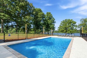 A rectangular swimming pool with a black fence, surrounded by trees and a clear sky. - Ultimate Lakefront Cabin with Outdoor Pool in Georgia (Eatonton)