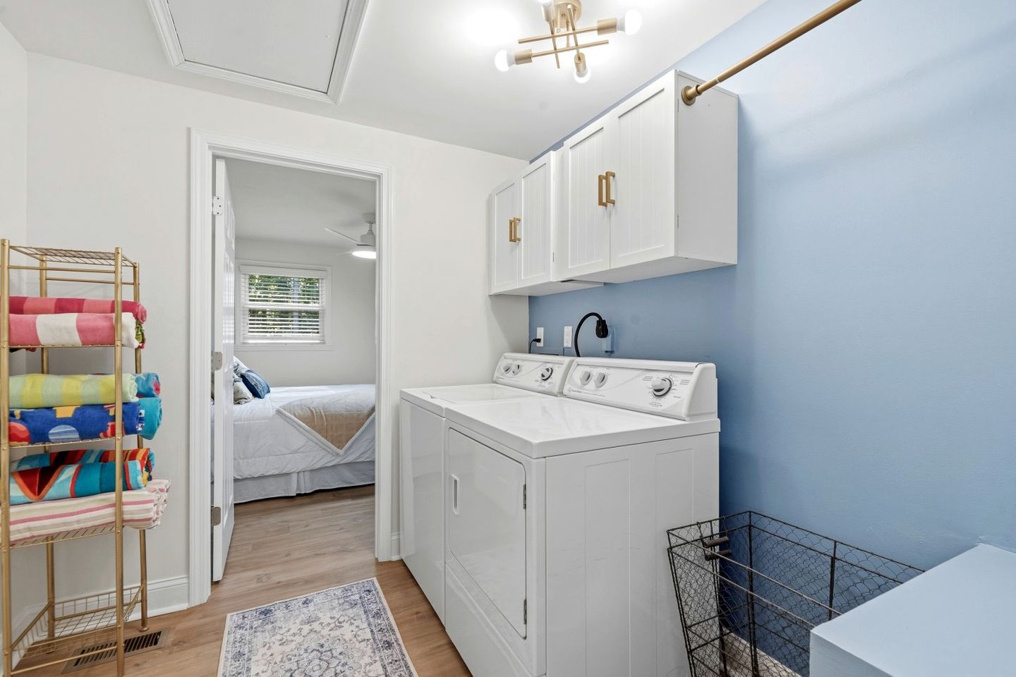 Een kleine wasruimte met een wasmachine, een droogrek, en een bed in de aangrenzende kamer.