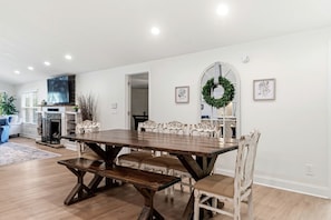 A dining area with a wooden table and white chairs, a fireplace, and a television.