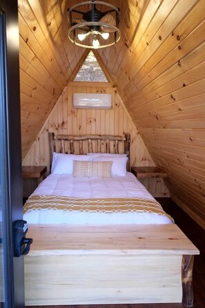 A wooden interior with a bed, a ceiling fan, and a window.