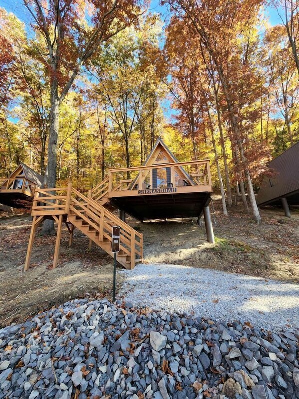 A wooden cabin with a staircase, labeled 'SHENDOAH,' surrounded by autumn trees.