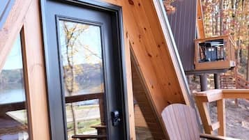 Eine Holzterrasse mit einer Tür, zwei Adirondack-Stühlen und einem Vogelhaus.