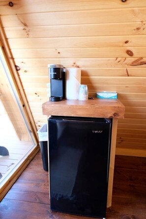 A compact black refrigerator with a U-MAX logo, a coffee maker, a white mug, and a box on a wooden countertop in a cabin with wooden walls and a window. - Lovely Rural Cabin Nestled Among Nature by Tappan Lake in Ohio (Deersville)