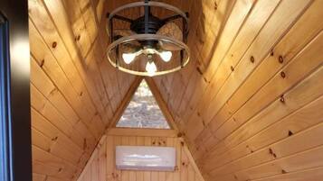 A wooden interior with a bed, a ceiling fan, and a window.