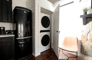 A compact kitchen with a black refrigerator, two washing machines, a wooden cabinet, and a chair. - Hygge Hollow Cabin on Fightingtown Creek in Blue Ridge, GA (Blue Ridge)