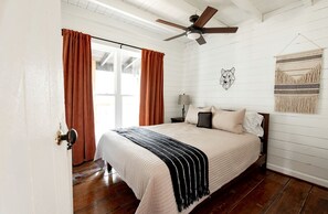 Un dormitorio con una cama, cortinas, ventilador de techo, lámpara de pared y un tapiz de macramé.