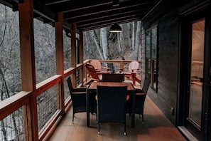 A wooden deck with a table and chairs, a hanging light fixture, and a view of trees.