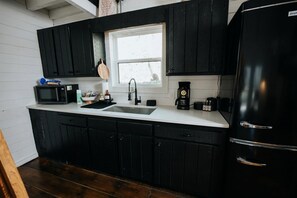 A kitchen with black cabinets, a white countertop, a sink, a microwave, a coffee maker, and a refrigerator.