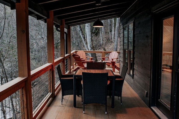 Une terrasse en bois avec une table et des chaises, un luminaire suspendu et une vue sur les arbres.