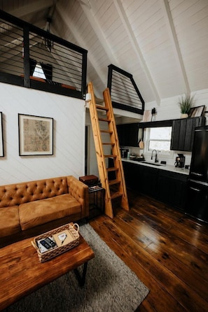 Un espace de vie de style loft avec une échelle en bois, un canapé en cuir marron, un coin cuisine et un escalier.