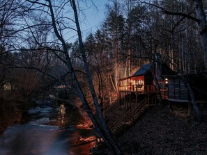 A cabin with a wooden deck and a river in the background.