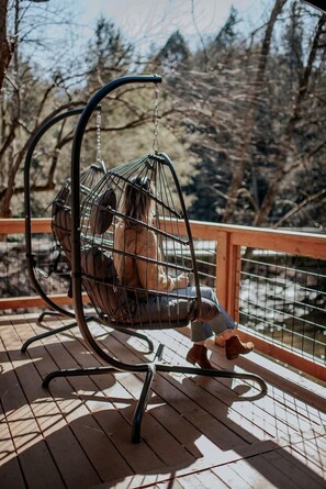 A wooden deck with a metal swing chair. - Hygge Hollow Cabin on Fightingtown Creek in Blue Ridge, GA (Blue Ridge)