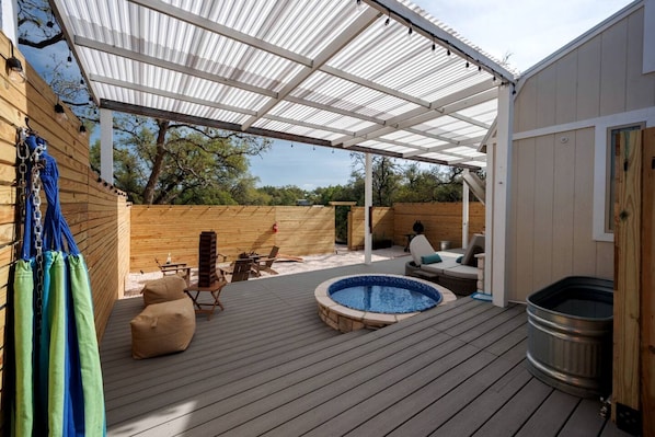 A covered outdoor deck with a hot tub, seating area, and a wooden fence.