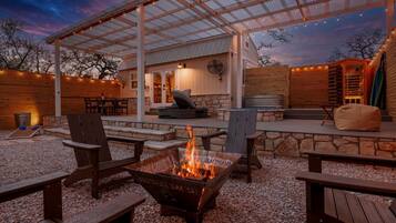 A covered outdoor patio with a fire pit, seating, and a stone wall.