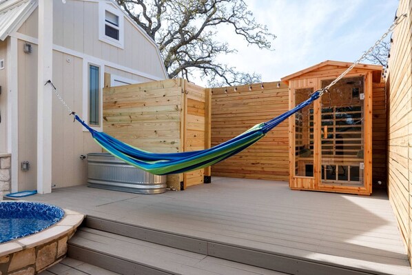 A hammock on a wooden deck, a hot tub, and a wooden structure with a window.