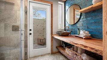 A bathroom with a glass shower enclosure, a wooden vanity with a bowl sink, and a blue-tiled wall.