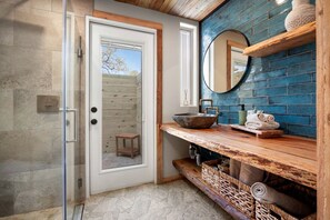 A bathroom with a glass shower enclosure, a wooden vanity with a bowl sink, and a blue-tiled wall.