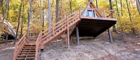 A wooden cabin with a staircase leading to a deck, surrounded by trees.