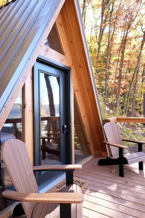 A wooden deck with two Adirondack chairs, a glass door, and a view of trees. - Romantic A-frame Cabin Ideal for Two by Tappan Lake in Ohio (Deersville)