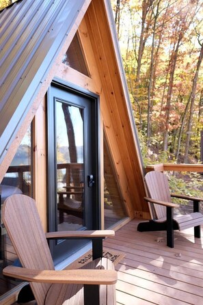 A wooden deck with two Adirondack chairs, a glass door, and a view of trees.